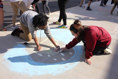 Students write messages of positivity with chalk on the sidewalk for a Chalk about Mental Health Campaign. 