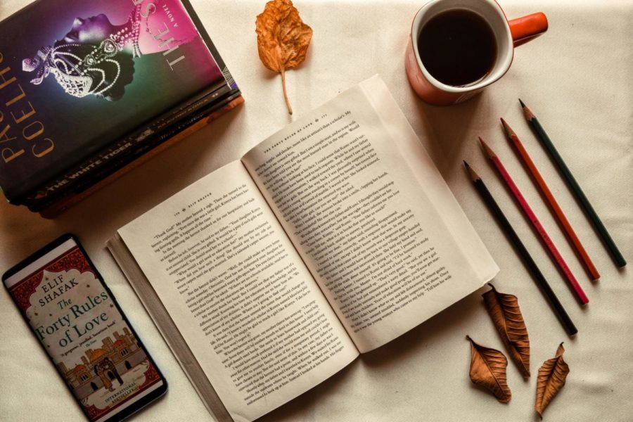 A scene with an open book, coffee, pencils, and leaves scattered around. 
