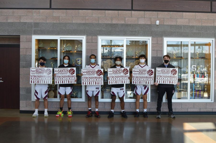 From left to right, Stroudsburg varsity basketball seniors Daniel Bruzzesse, Alexander Santos, Justin Shenery, Jahkai Barnes, Kevin Duffy, and Daniel Mercurio stand before a game with their posters. 