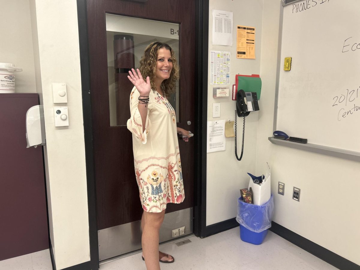 Ms. Lobasso poses at the door of her classroom, waving goodbye to her students.
