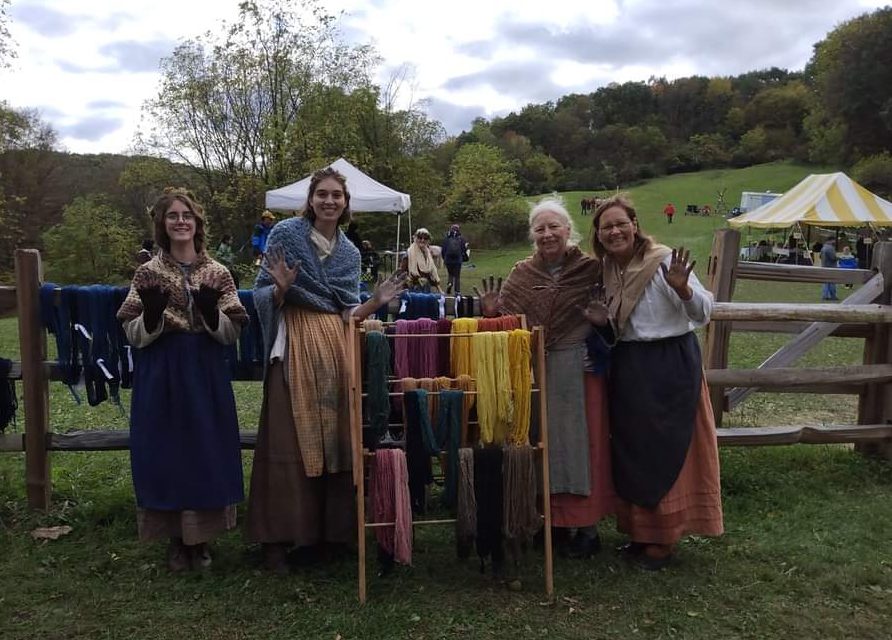 A group of women standing by a rack of naturally dyed yarn spun by a spinster on the farm (2023). Photo submitted by D. Porter or Quiet Valley Farms. 
