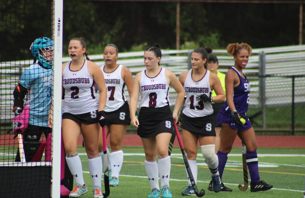 The field hockey team works together to perform a corner.