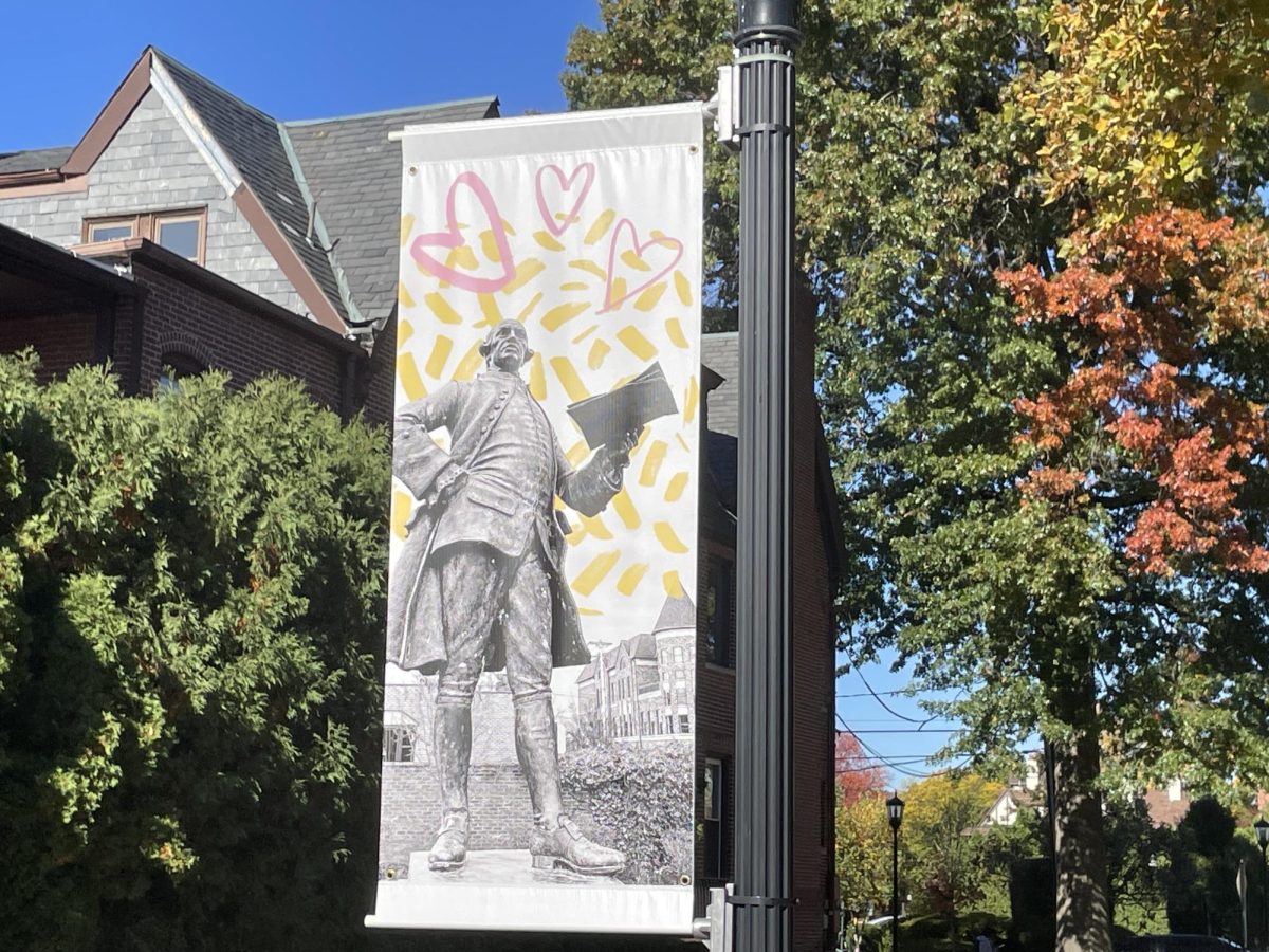 A sassy looking statue of a man decorated with hearts and fireworks on the banner on the Wilkes campus. 