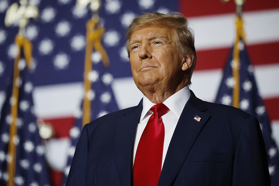 Donald Trump, the 45th and 47th President of the United States of America, looks onto his crowd while standing in front of the American flag.