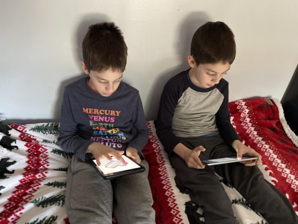 Two young boys sitting together while playing games on their iPads. 