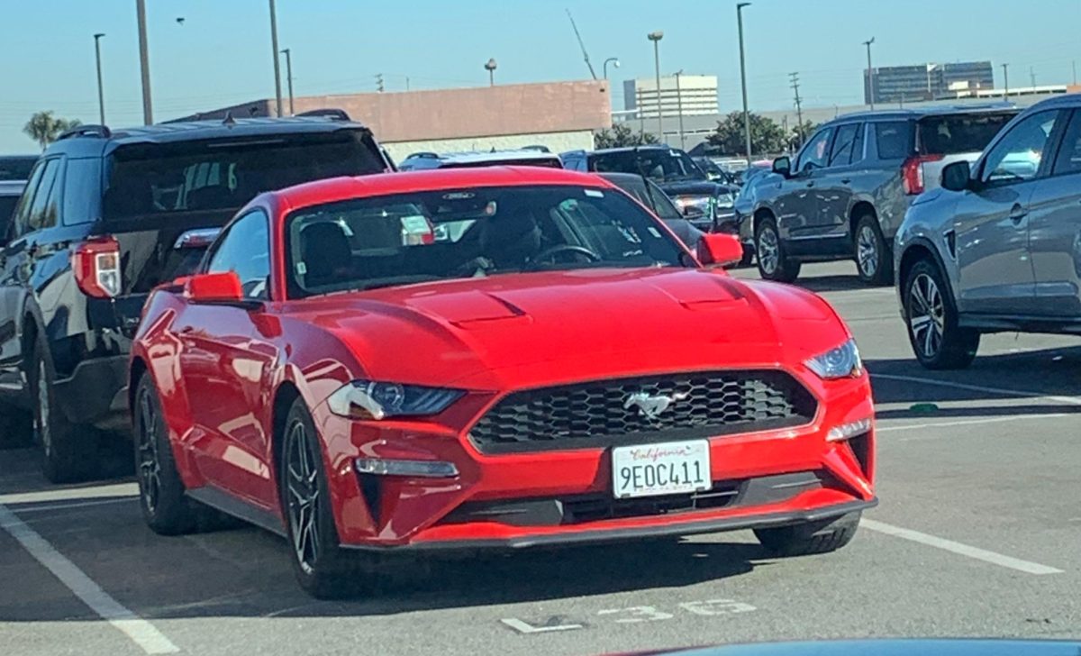 A red Mustang  in a parking lot  surrounded by other cars. 