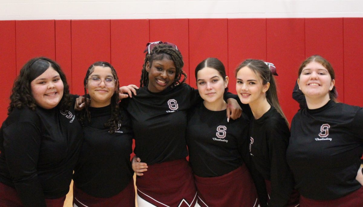 Cheerleaders Colleen, Leslie, Tiana, Molly DeRosa, Baylee, and Sophia pose for a picture at a basketball game. 