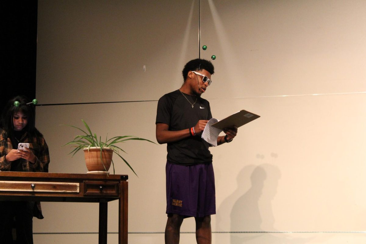 "LeBron James" played by Noah Charles, '25, reads off a clip board while answering questions. 