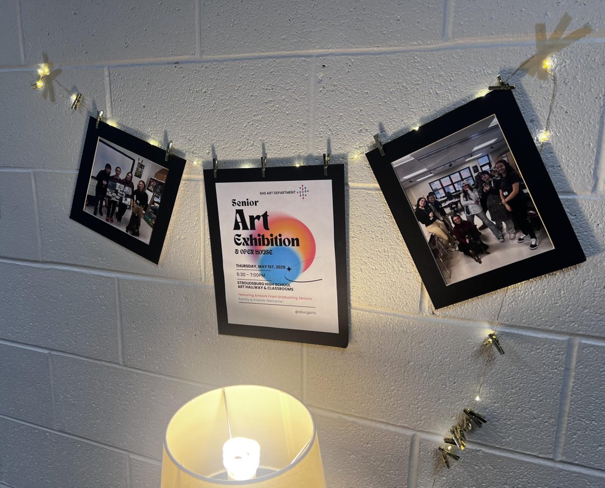 "Senior Art Exhibition" flyer with photos of students hung next to the art room. Being one of the first things seen as you walk to view the pieces of art.