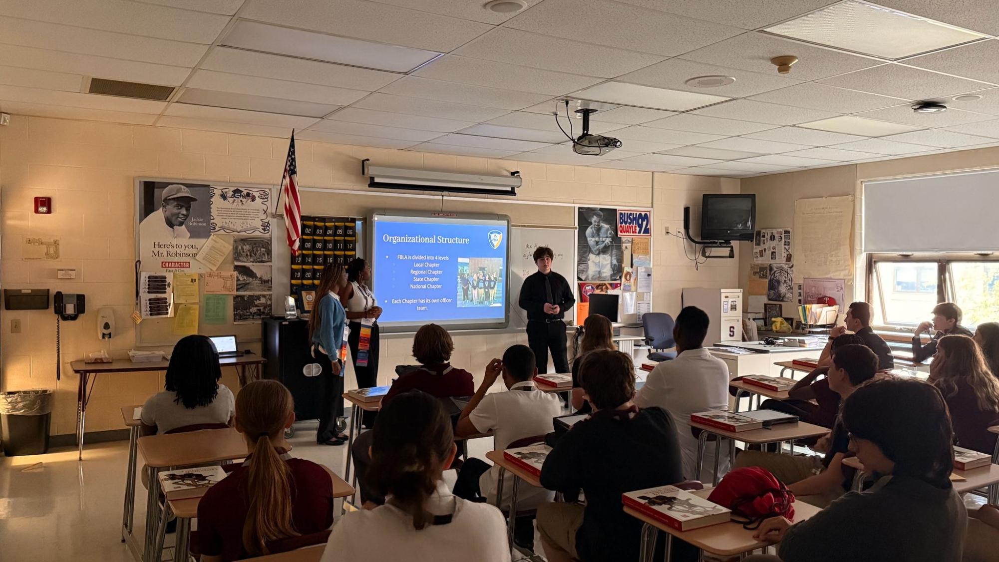 Nichole Ogwu, '27, Zoey Charles, '27, and Jacob Pachter, '27, explaining FBLA in a presentation to the freshmen at the SJHS.