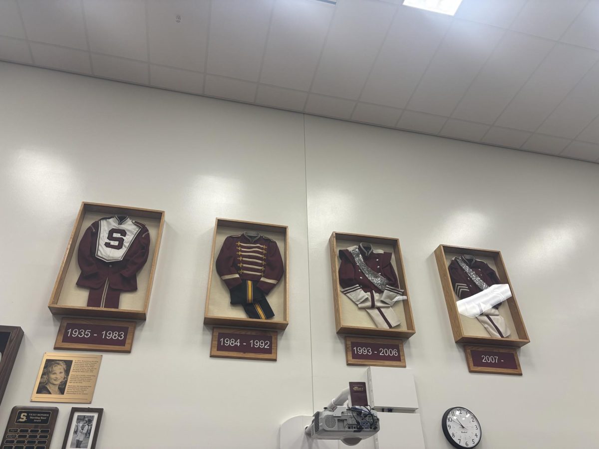 A picture of the past uniforms of the Marching Band displayed on a wall in the band room.