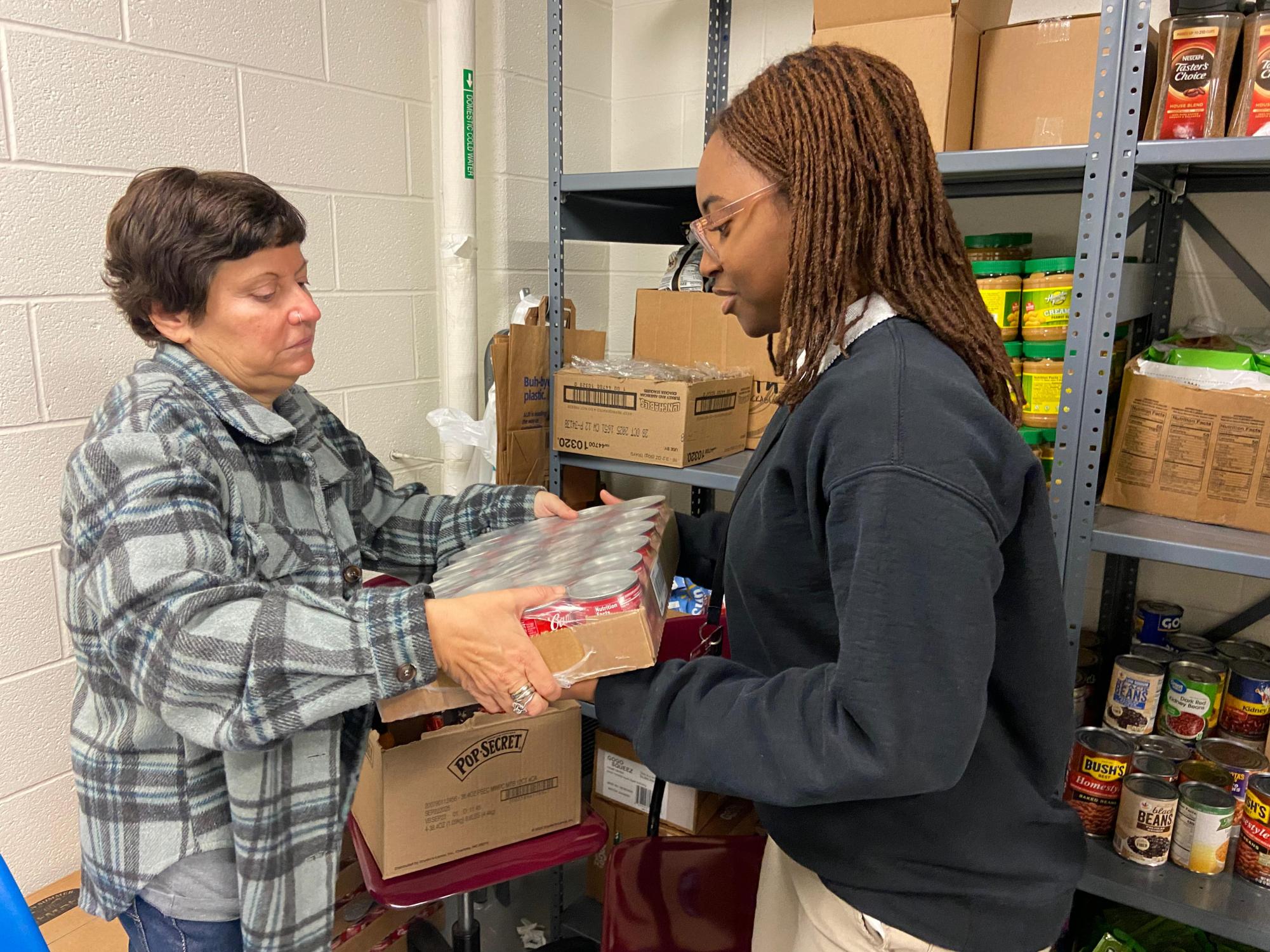 Mrs. Austin handing an FBLA member some cans that need to be organized on the shelves.