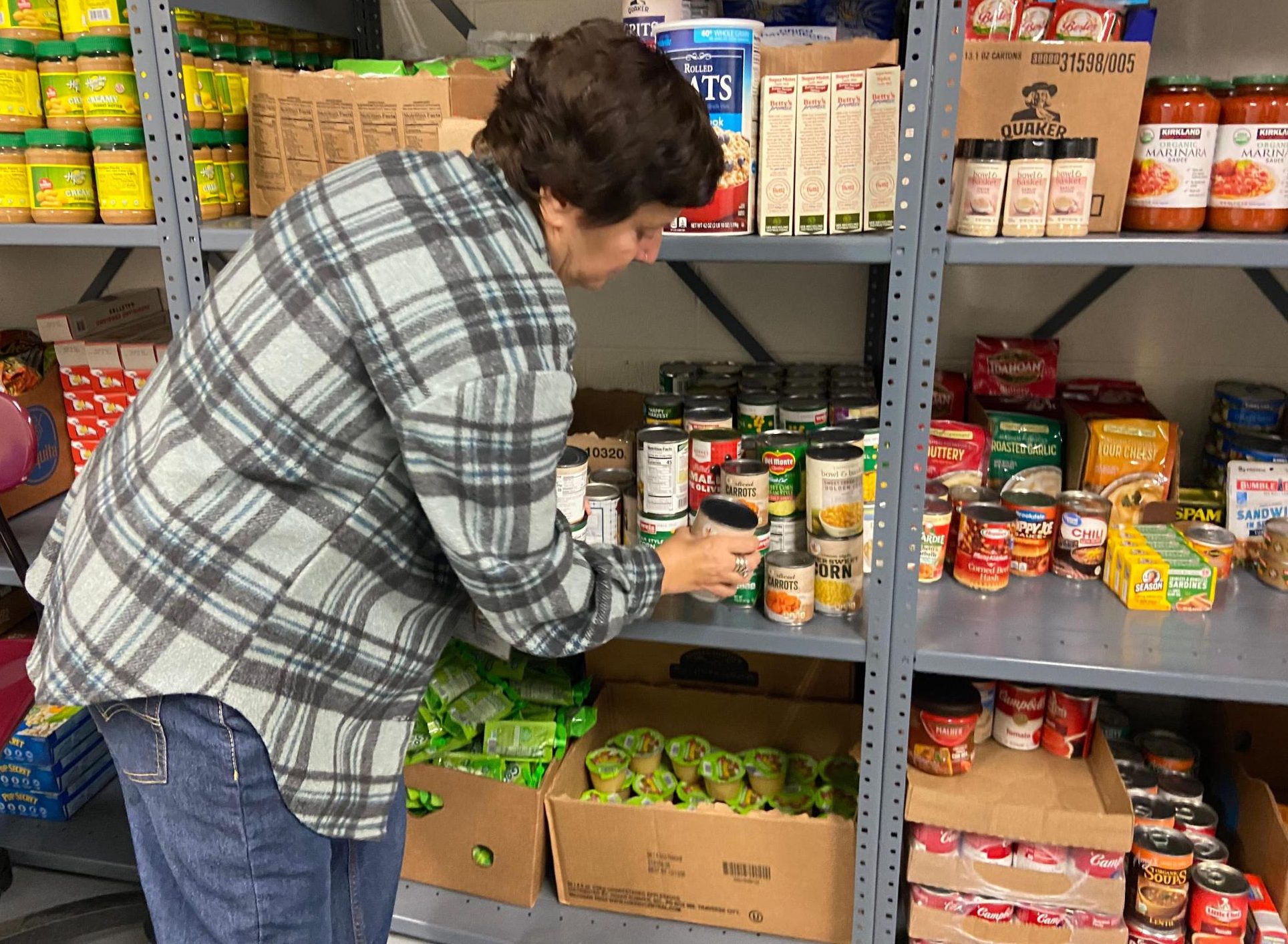 Mrs. Austin, the teacher who is in charge of the food pantry, checking some cans on the main shelves.