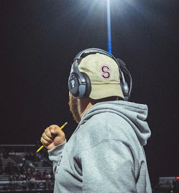 Coach Dom watches the football game from the sidelines.