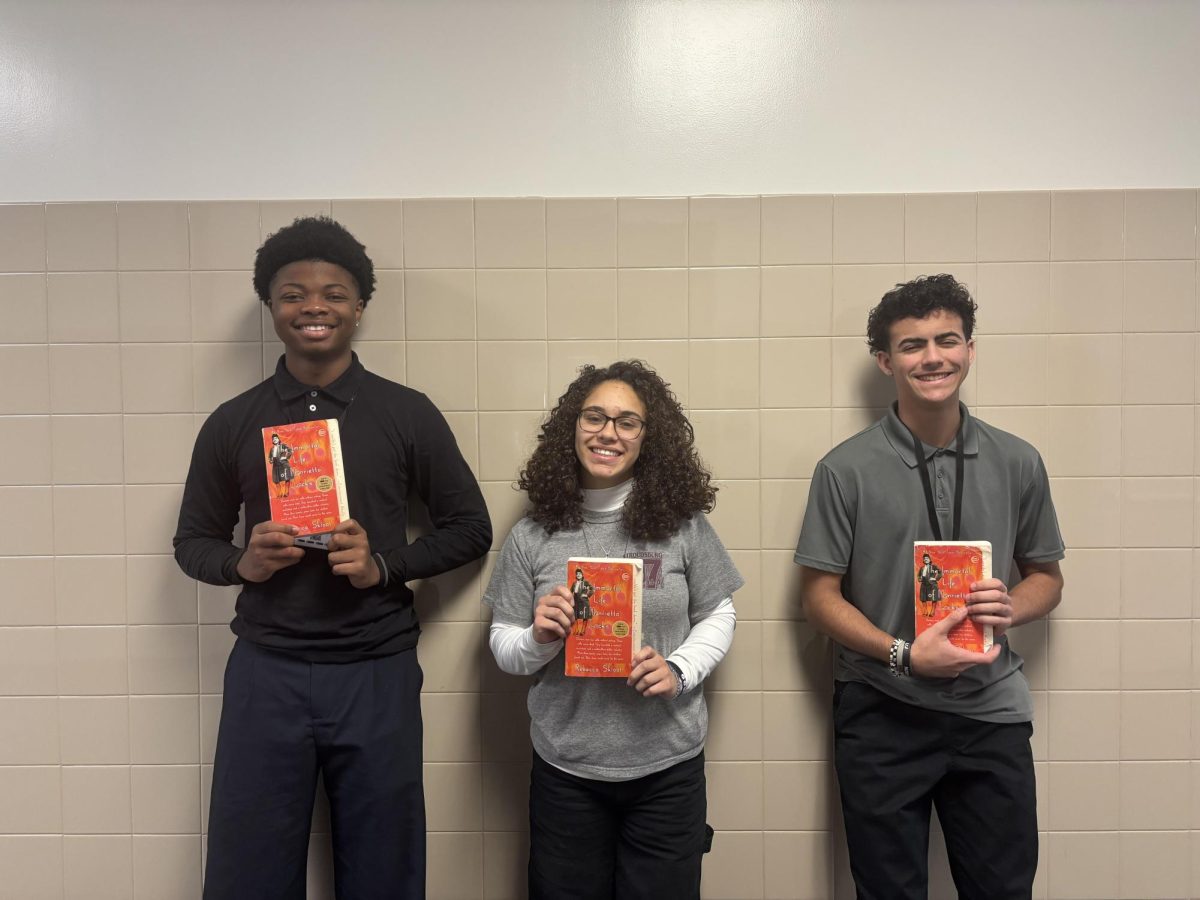 Kyle Youman '28, Karly Evans '28, and Aj Roman '28 posing for a picture with the book "The Immortal Life of Henrietta Lacks."