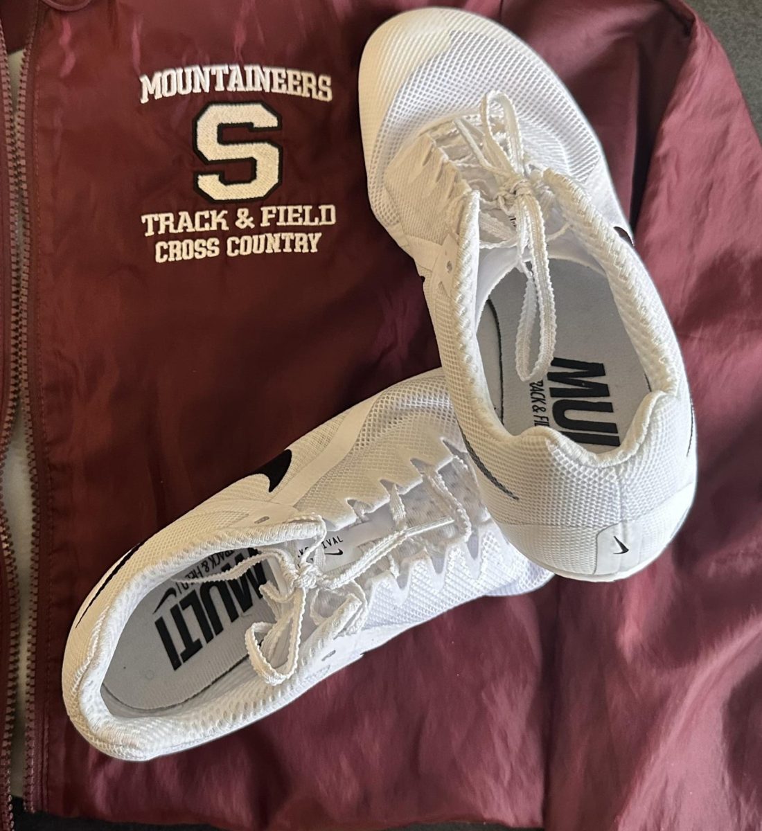A pair of Nike spikes on top of a Strousburg High School Track and Field Windbreaker.